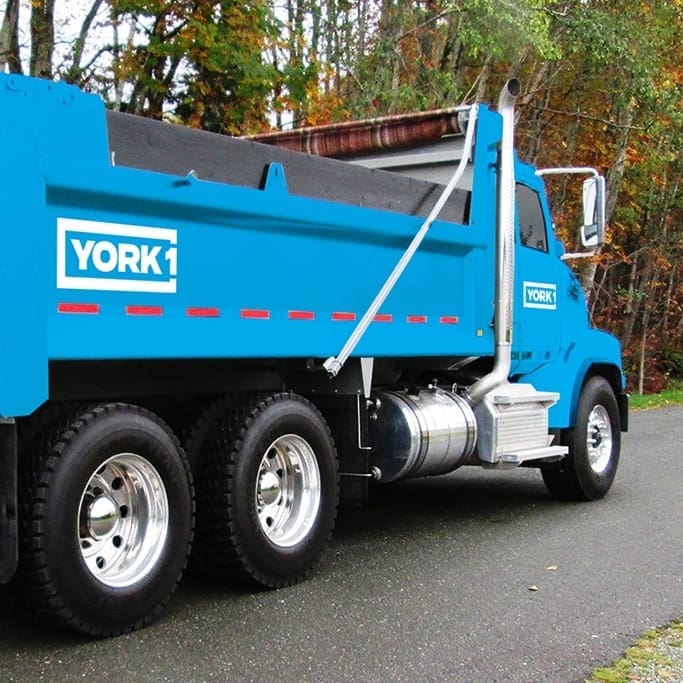 Blue York1 dump truck driving on tree-lined road