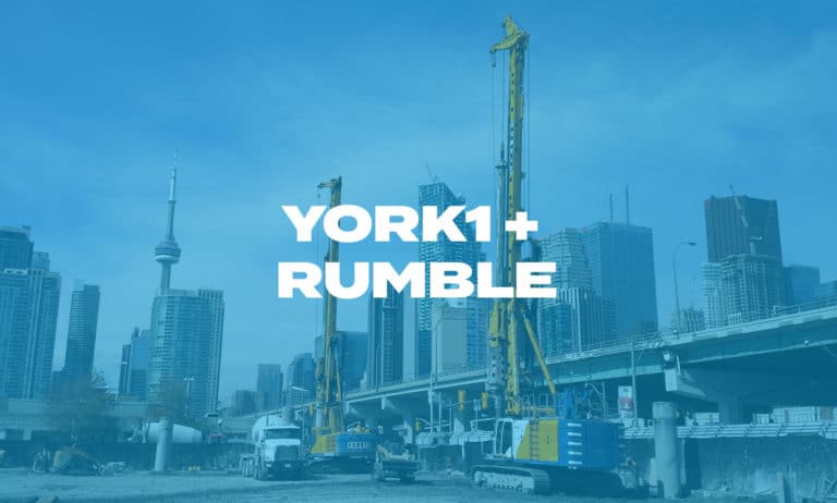 Two hydraulic rigs completing a shoring job with the CN tower and skyscrapers in the background. Photo with blue overlay, York1 + Rumble in white text.