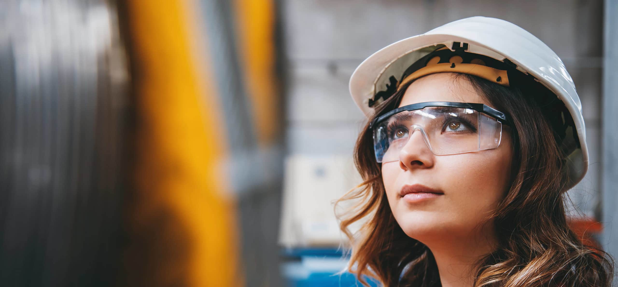 Headshot of worker on a job site looking up. Wearing white hardhat and clear goggles.