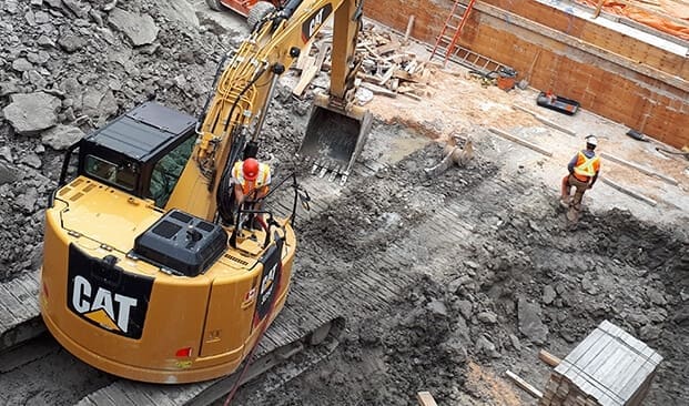 Two workers and excavator completing a job on construction site.