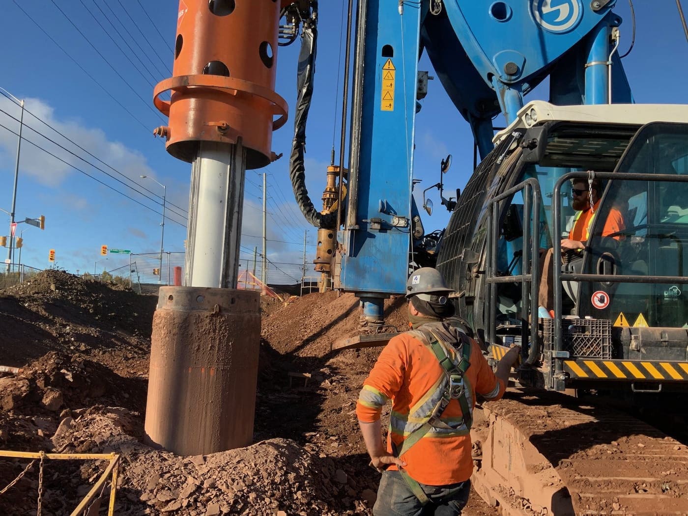 Two workers using a hydraulic drill rig to complete a shoring project