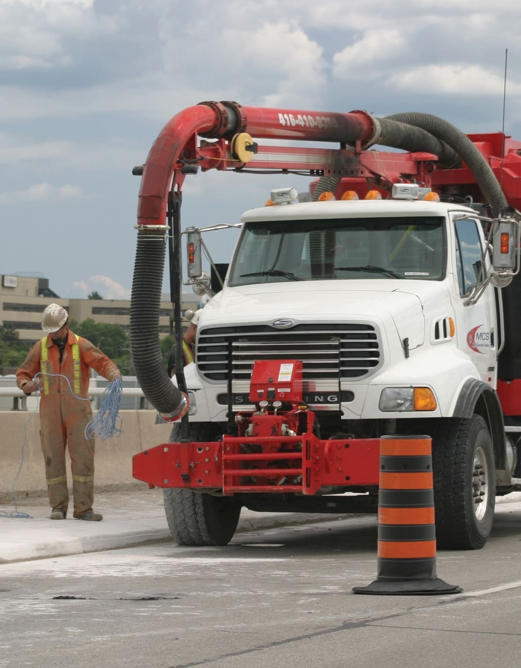 A red and white hydrovac truck parked on a highway road. Worker beside the truck preparing to hydrovac the site