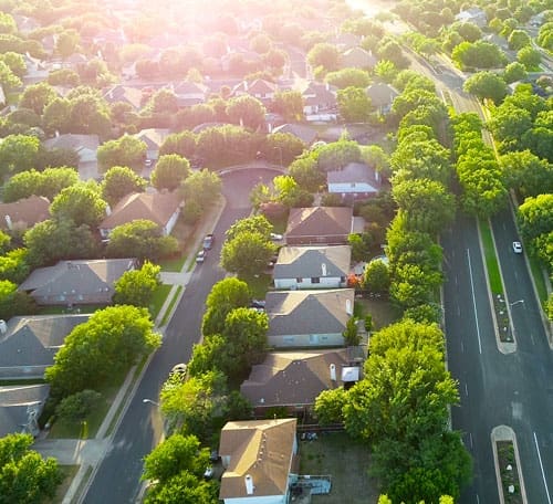 Bird's-eye view of a residential neighbourhood. Houses, cars and tree-lined streets.