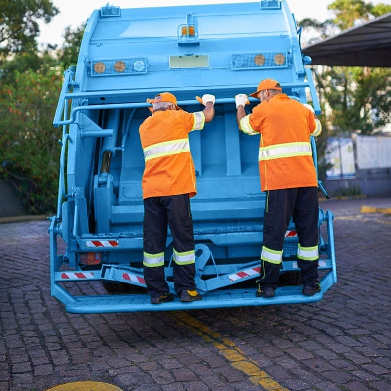 Two uniformed workers on the back of a blue recycling truck