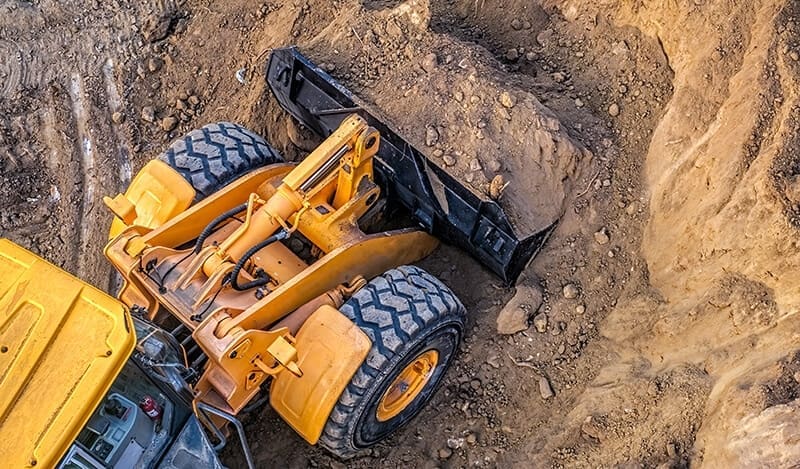 Yellow earth mover digging into a dirt pile