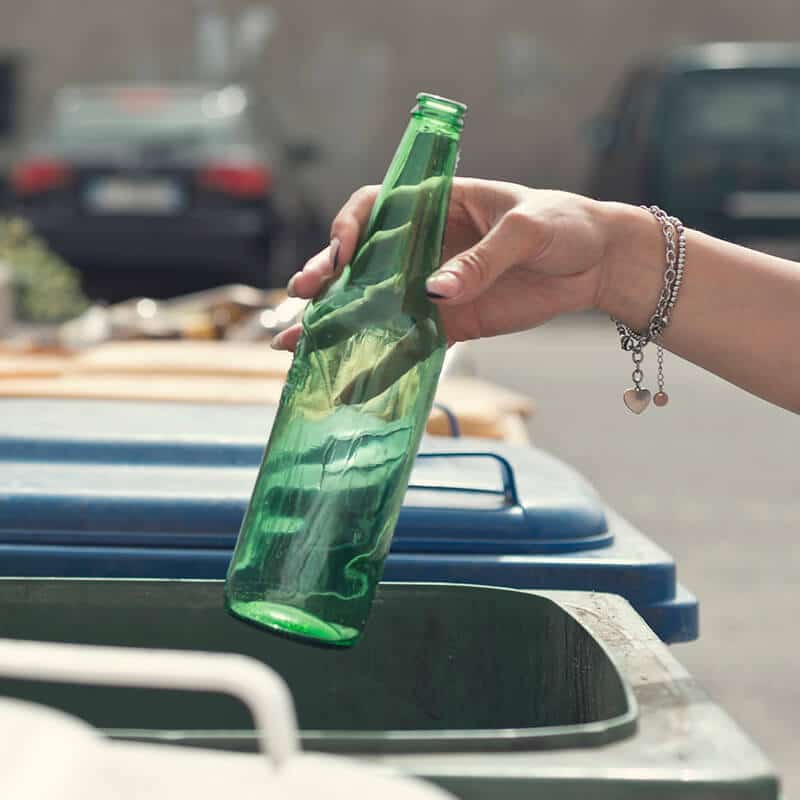 Hand placing a green glass bottle in a recycling bin