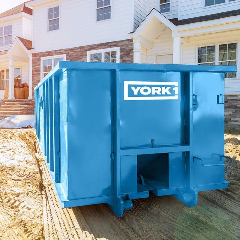 Blue York1 roll-off bin on a dirt driveway in front of a house 