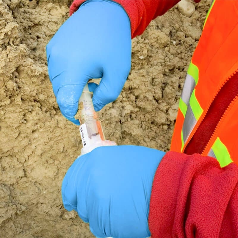 Hands wearing blue gloves conducting a soil test over a pile of soil