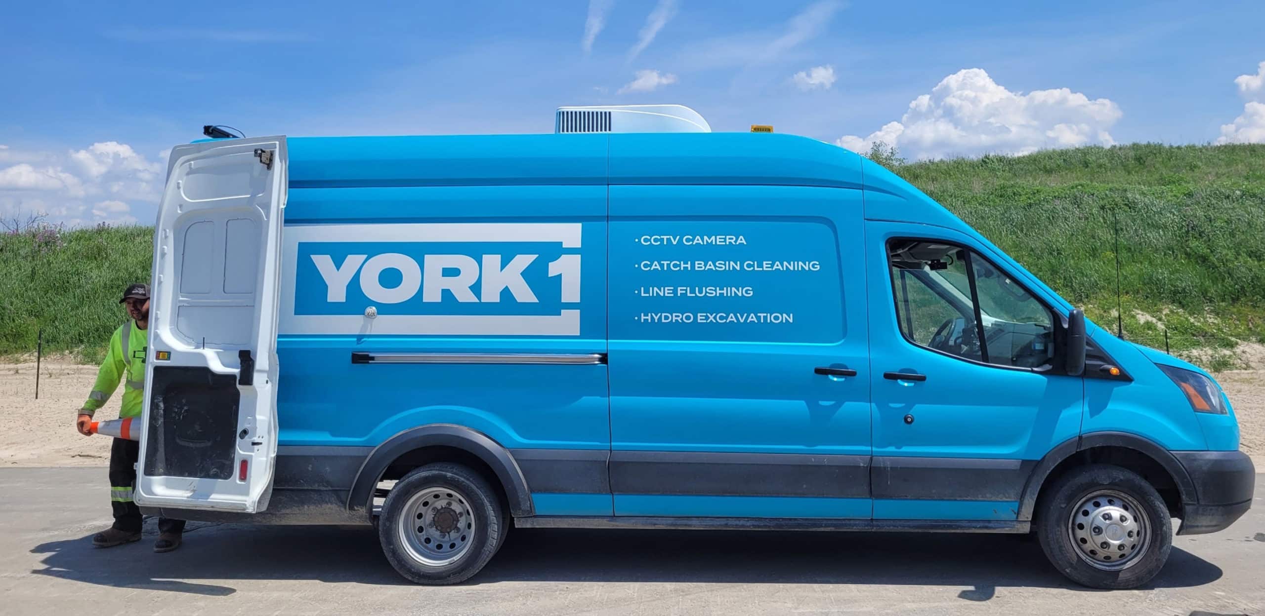 A York1 sprinter truck with the back doors open and an employee holding cable.