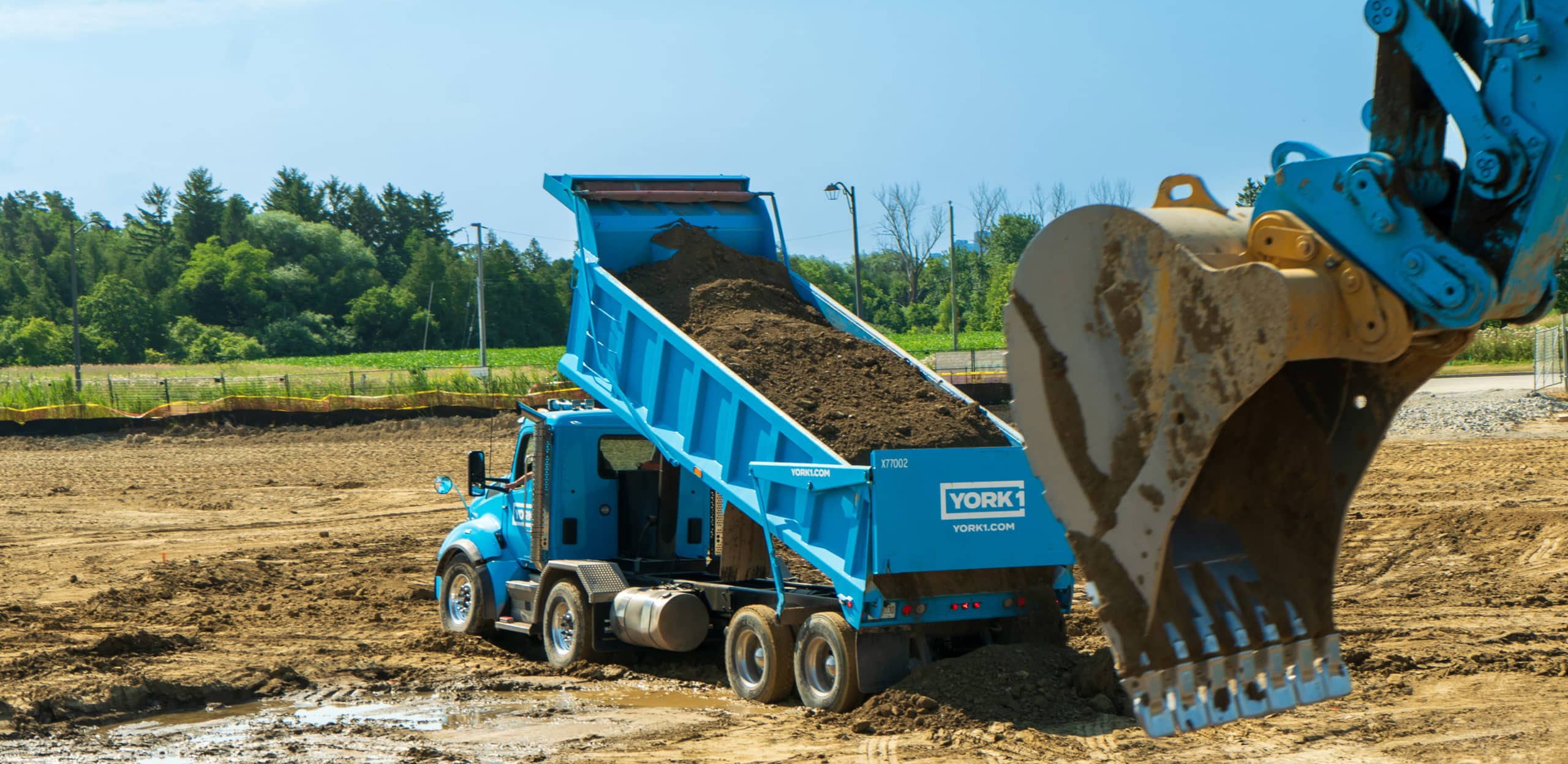 A cyan York1 dump truck is unloading clean soil on a job site.