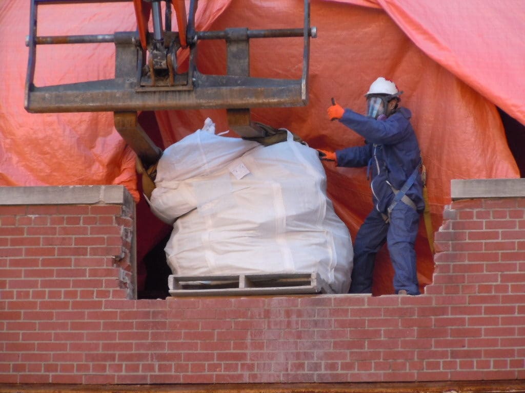 A person working with a machine operator to load up a bag of hazardous waste