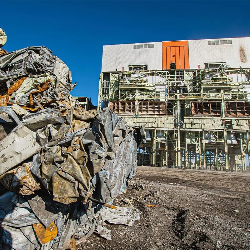 Demolition preparation of the last building of the former OPG plant, with a pile of scrap metal in the foreground stacked for asset recovery